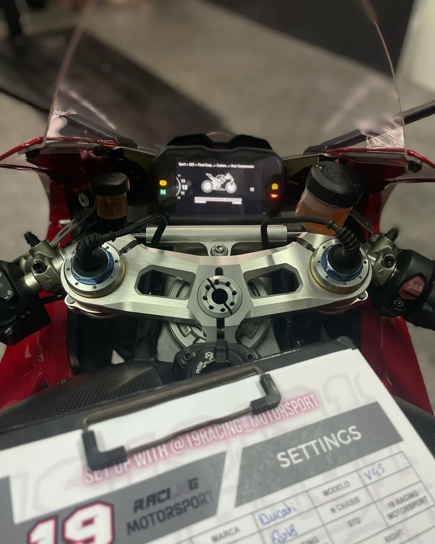 Cuadro de mandos de una superbike roja con la hoja de reglajes del taller apoyada delante