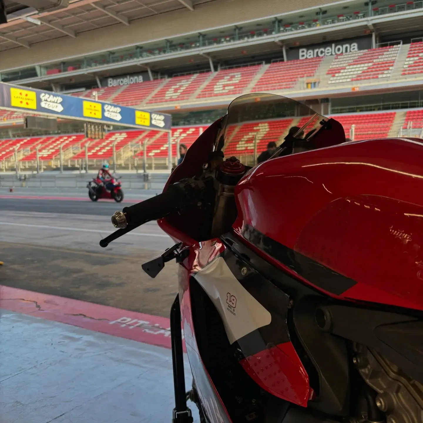 Moto de competición roja en el pit lane del circuito de Montmeló, con la tribuna al fondo