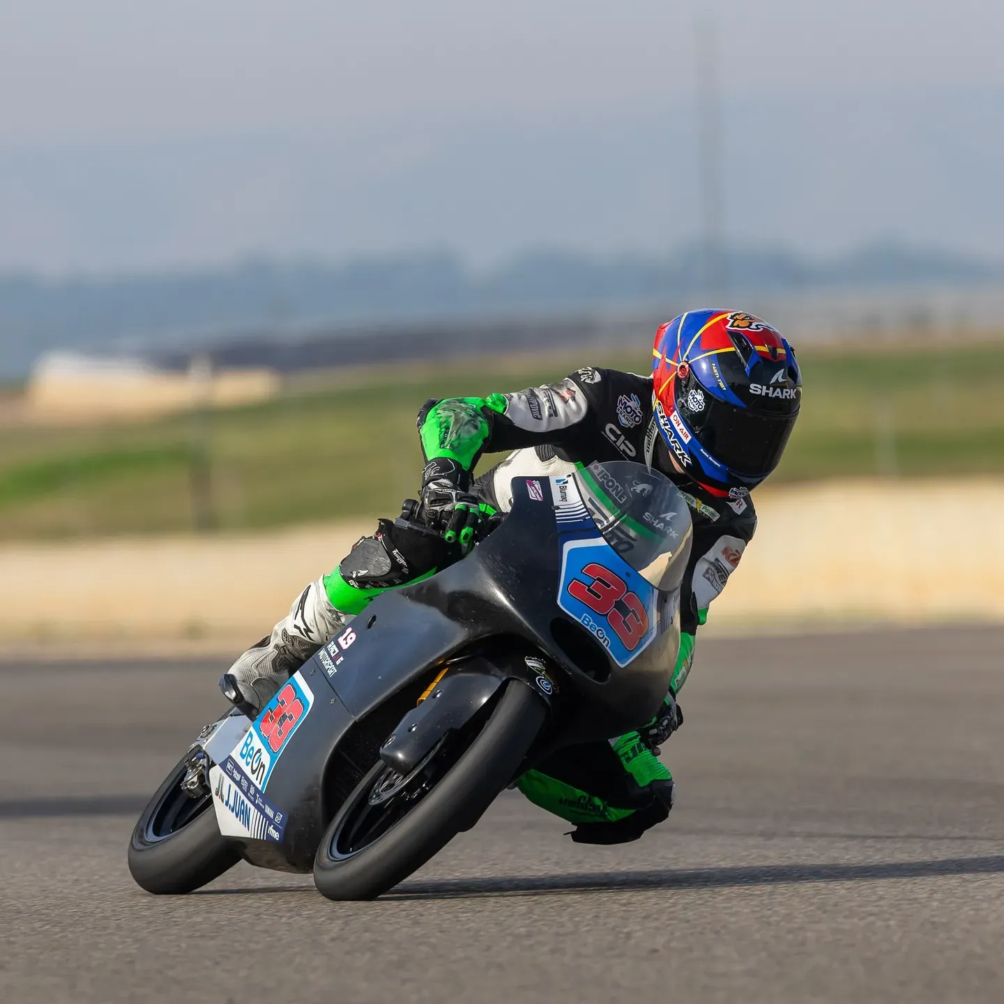 Piloto con mono verde tumbado en una curva con una moto de competición de carenado gris