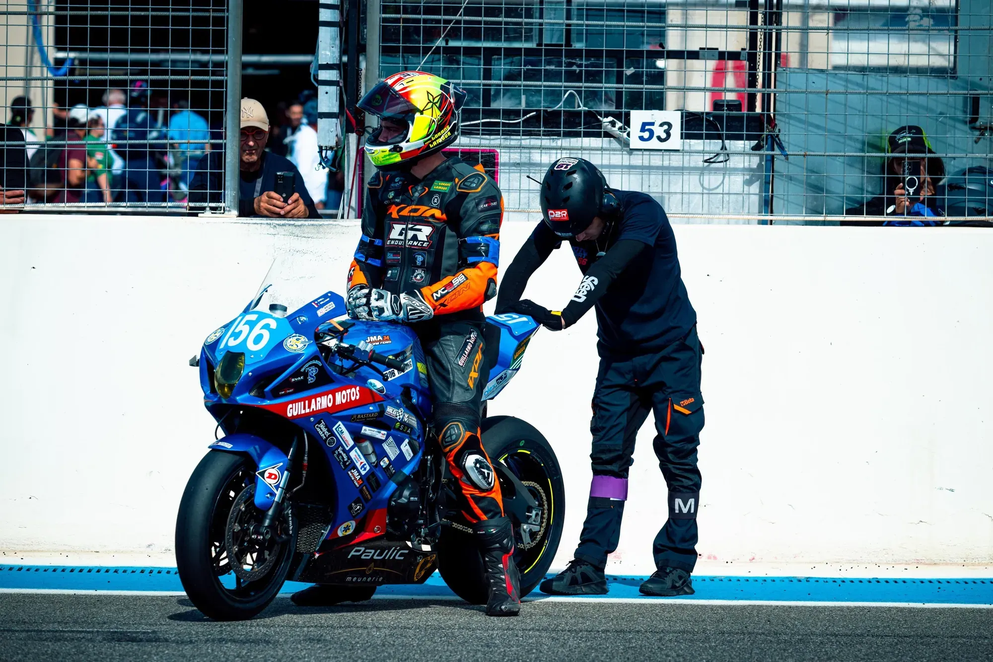 Piloto sobre una moto azul de resistencia en el pit lane, con un mecánico ayudándole antes de salir a pista
